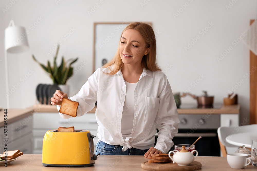 Mature woman making tasty toasts in kitchen Mature woman making tasty toasts in kitchen