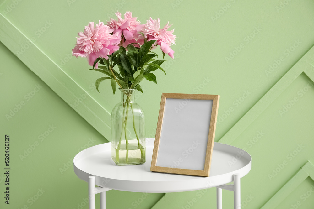 Blank photo frame and vase with bouquet of beautiful peony flowers near green wall Blank photo frame and vase with bouquet of beautiful peony flowers near green wall