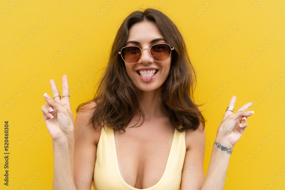 Young beautiful woman. Carefree woman posing in the street near yellow wall. Positive model outdoors in sunglasses. Happy and cheerful showing v sign Young beautiful woman. Carefree woman posing in the street near yellow wall. Positive model outdoors in sunglasses. Happy and cheerful showing v sign