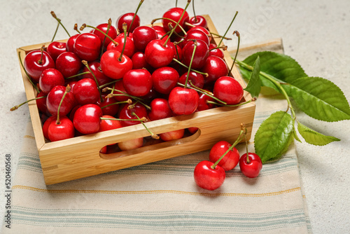 Wooden box with sweet cherries on light background