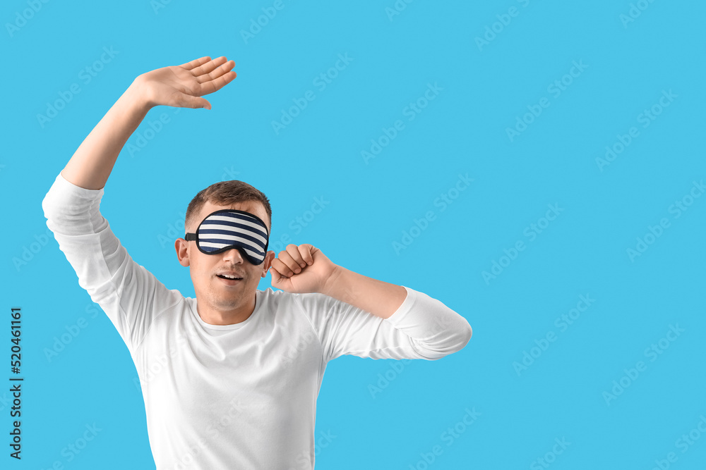 Naklejka premium Young man with sleeping mask stretching on blue background