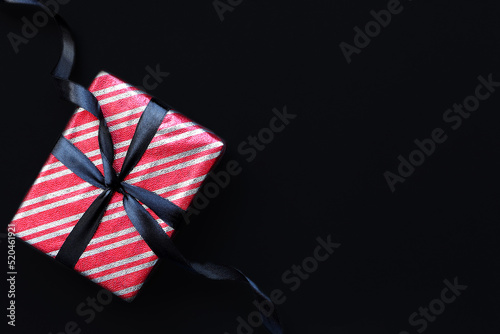 Gift box wrapped in red striped paper and tied with black bow on black background. Space for text.