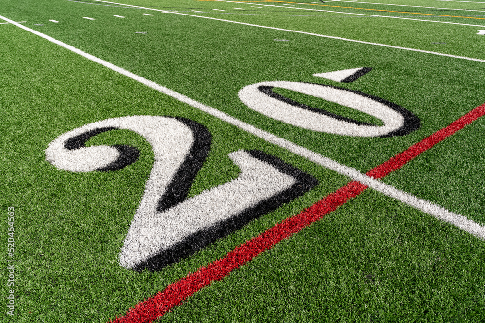 Synthetic turf  slanted football 20 yard line in white with black number shadow along with red lacrosse line and yellow soccer mid field line	