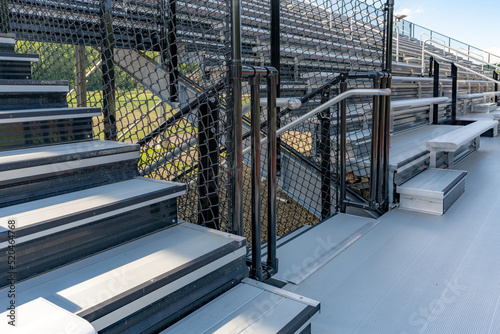 Exit, entrance, vomitorium at empty metal stadium bleacher seats along aisle with steps and railing.
