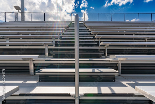 Looking up at anticipation of climbing exterior stadium bleacher stairs with a sun star near the top with clouds. 