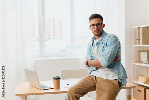 Self-confident narcissistic handsome stylish young businessman in eyewear cross hands look at camera sitting on office table. Copy space for ad. Remote Job, Technology And Career Profession Concept