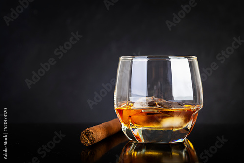 Glass of whiskey and cigar on dark background.