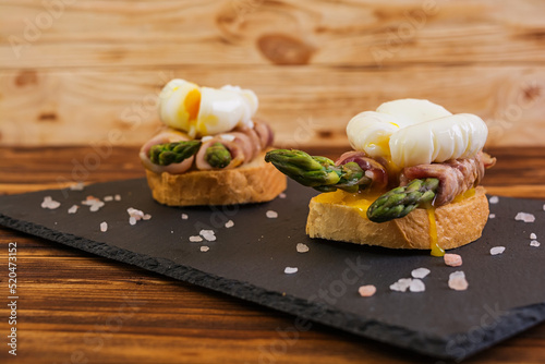 Grilled toast with asparagus in bacon and poached egg on wooden background