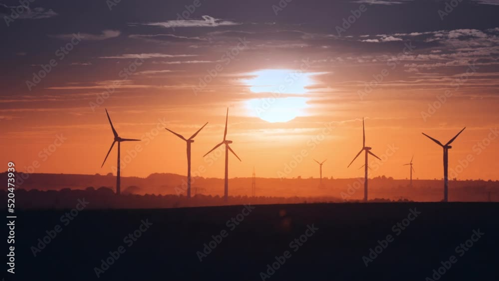 Wind turbines in the fields of wheat at the sunset. Dark clouds in the vibrant orange sky. Slow-motion. Wind turbines in the fields of wheat at the sunset. Dark clouds in the vibrant orange sky. Slow-motion.