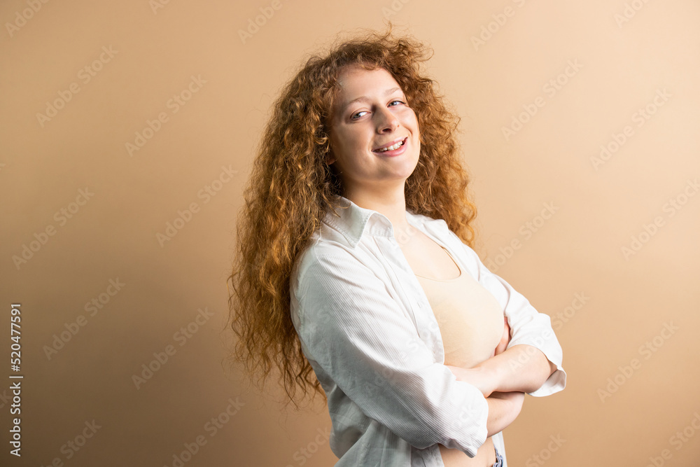Self-confident redhead woman looking at the camera with crossed hands posing over the golden background and copy space. Self-confident redhead woman looking at the camera with crossed hands posing over the golden background and copy space.