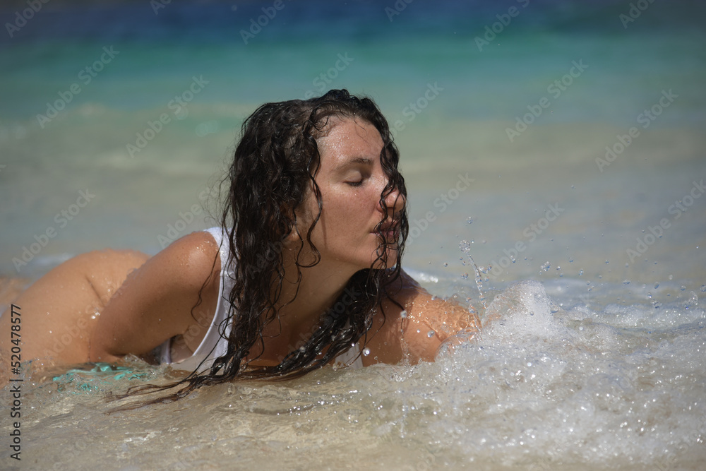 A portrait of brunette girl in swimsuit swimming in water. Portrait of sexy female in a white bikini on a tropical beach. A curly woman enjoys during her summer holiday in the Philippines