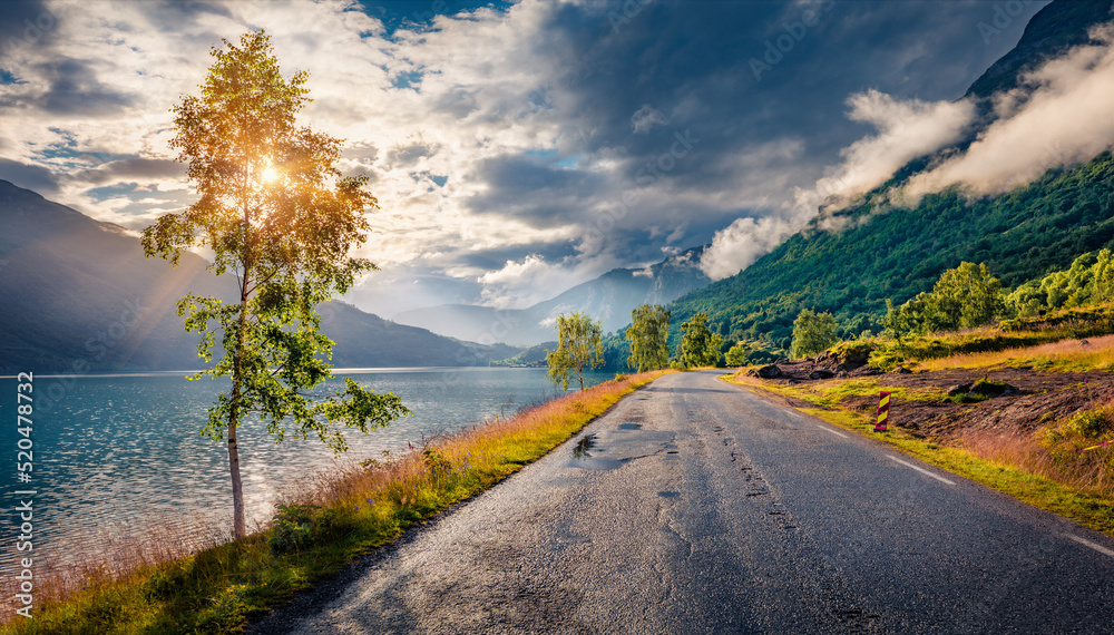 Fototapeta premium Dramatic summer view of Lovatnet lake with asphalt road. Foggy morning scene of Sogn og Fjordane county, Norway, Europe. Traveling concept background..