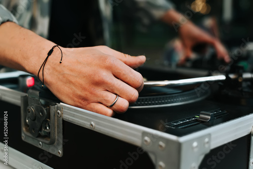 Close-up of DJ mixing vinyl records on turntable at street music festival in evening. Selective focus on disjockey's hand