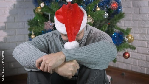 Crying Santa man in room. A view of crying stressed man in Santa hat on the floor during Christmas party. photo