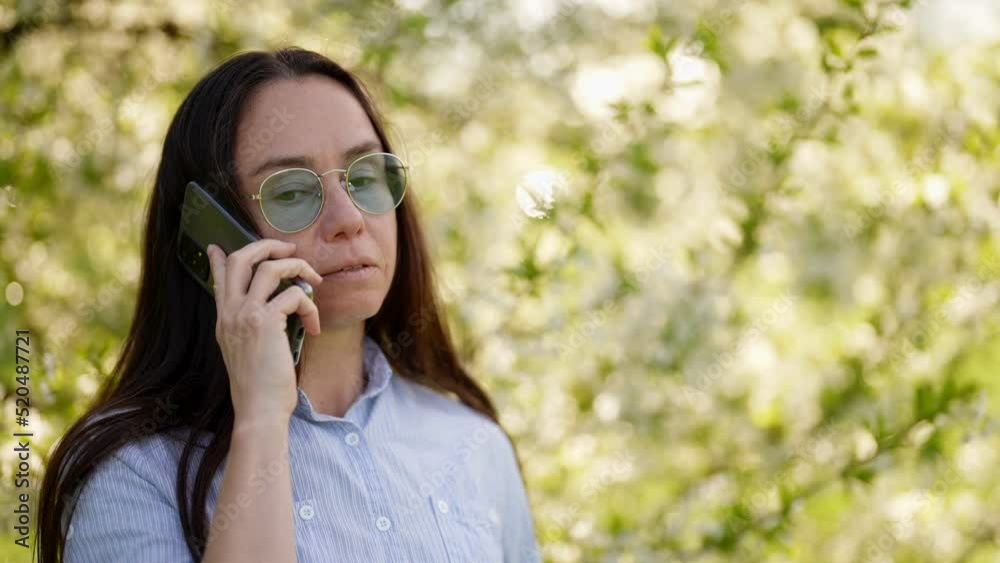 adult positive woman is talking by cellphone in blooming garden, portarit of pretty lady in spring adult positive woman is talking by cellphone in blooming garden, portarit of pretty lady in spring