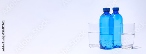 Blue plastic bottles and glasses of water on light background