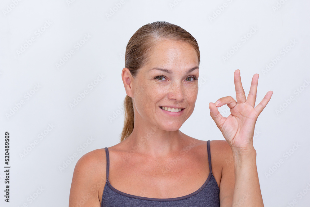 Portrait of caucasian middle aged woman of 40s showing OK as sign by fingers on white background looking at camera Portrait of caucasian middle aged woman of 40s showing OK as sign by fingers on white background looking at camera