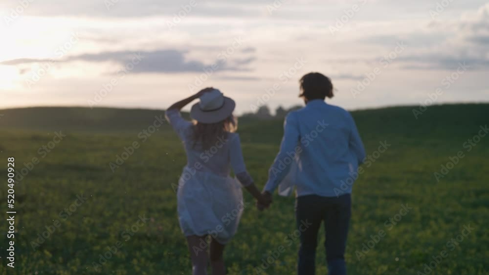 Sunset on a countryside, young couple in nature, man and a woman are running through a field of rapeseed holding hands, back view, 4k slow motion. Sunset on a countryside, young couple in nature, man and a woman are running through a field of rapeseed holding hands, back view, 4k slow motion.