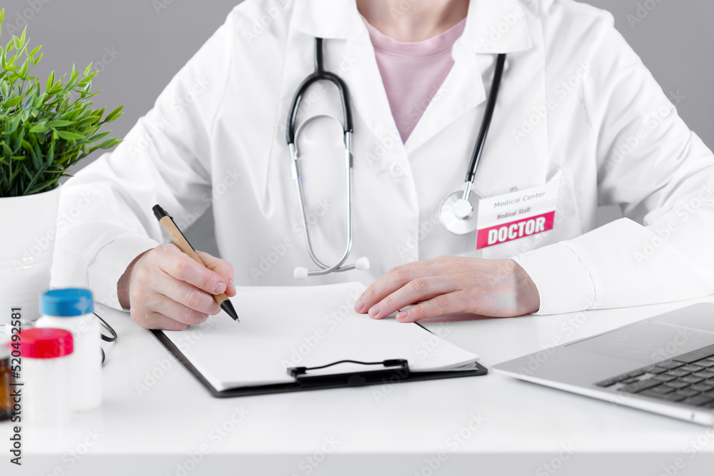 A doctor in a white coat makes a note on paper with a pen. A doctor in a white coat makes a note on paper with a pen.