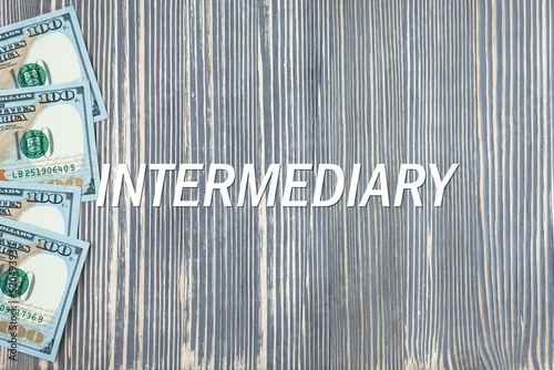 INTERMEDIARY - word (text) on wooden background, money, dollars. Business concept (copy space).