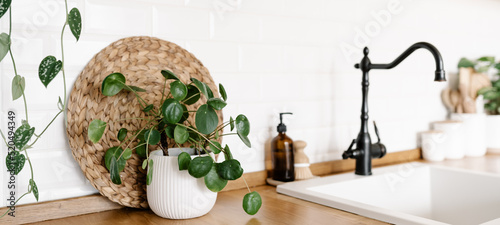 View on white simple modern kitchen in scandinavian style, kitchen details, houseplants in interior, wooden table, white ceramic brick wall background