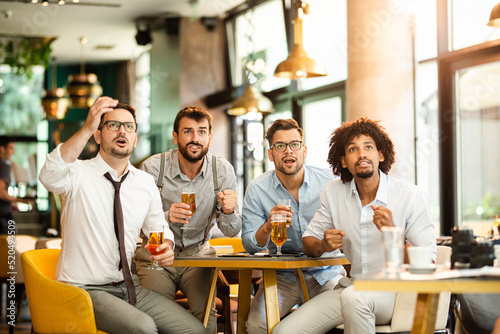 Cheerful old friends having fun and drinking draft beer at bar table in pub. photo