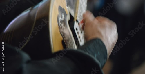 Close on man’s hands playing Greek bouzouki with dancers in background