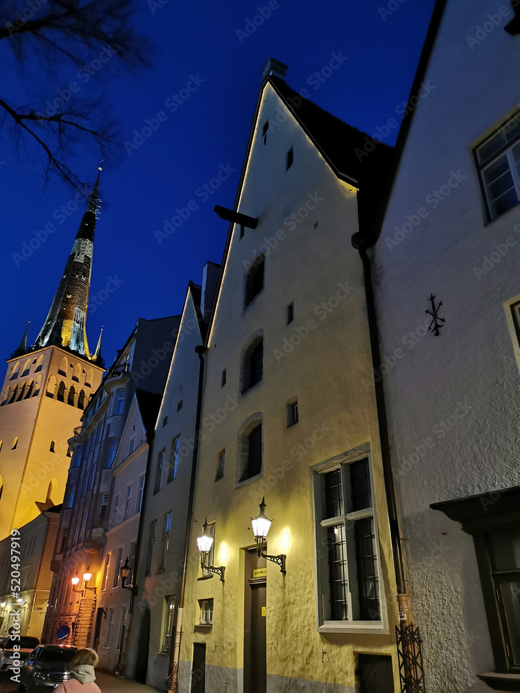 Naklejka premium Three brothers building complex and the St. Olaf Baptist Church on one of the streets of Old Tallinn against the dark blue sky. Spring evening.