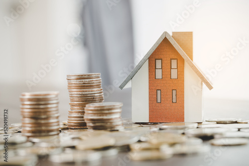 House model and money coins stacks on blur table background. Savings plans for home, loan, investment, mortgage, finance and banking about house concept.