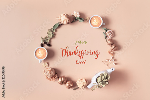 Autumn composition with Happy Thanksgiving Day greeting text. Wreath made of dried leaves and coffee cups on pastel beige background © Alina