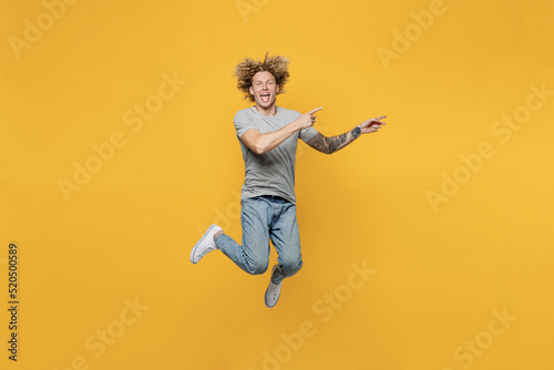 Full body young caucasian man 20s he wear grey t-shirt pointing index finger aside indicate on workspace area copy space mock up isolated on plain yellow backround studio. People lifestyle concept © ViDi Studio