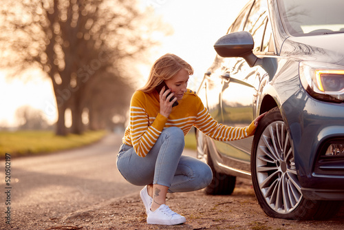 Woman Calling For Help On Phone After Car Breakdown On Country Road With Tyre Puncture photo