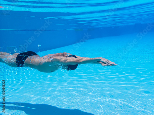 Athlete swimmer breathing out air bubbles, while diving, training in the blue waters of a swimming pool. Selective focus. Underwater concept. Sport, recreation, lifestyle concept.