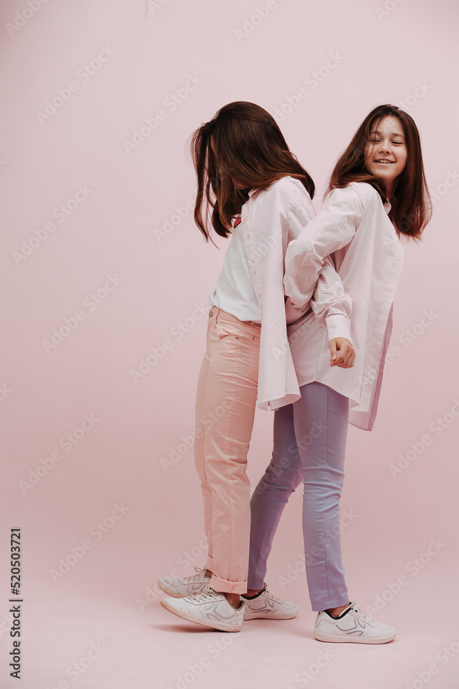 Playful twin girls stadning ack to back, stratching against one another for fun Playful twin girls stadning ack to back, stratching against one another for fun