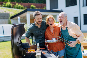Senior couple with adult son grilling outside on backyard in summer family during garden party