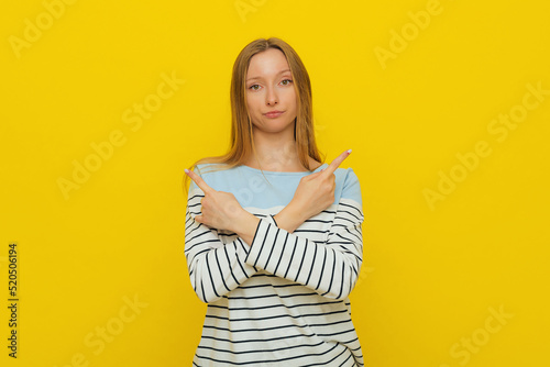 Choice  decision. Upset gloomy girl with fair-haired  sulking and frowning  pointing sideways  showing left and right  two ways  deciding  picking from variants  yellow background