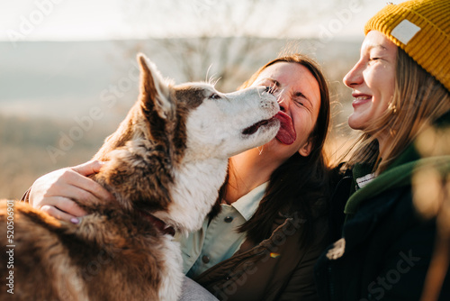 Two women hugging each other and enjoying the trip, walk with the dog in the nature autumn forest, fall season. Romantic family moments