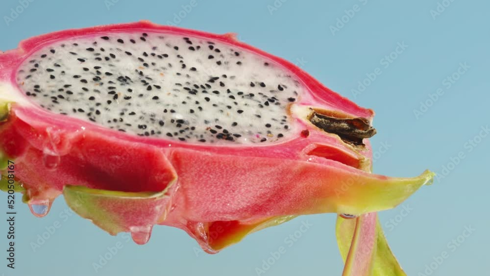 Half of a pitahaya with white flesh, a dragon fruit against a blue sky, drops of water are flowing down it.
