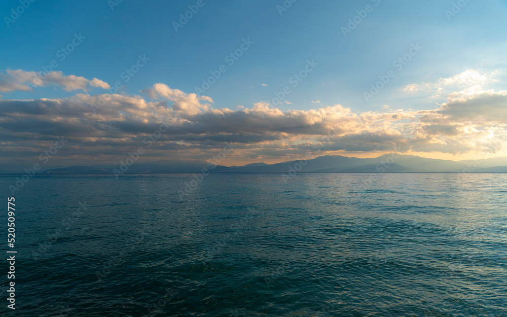 Cloudy sky above the sea and mountains in the horizon's background. The change of weather is continuous in all seasons. Calm, relaxing, scenic view.