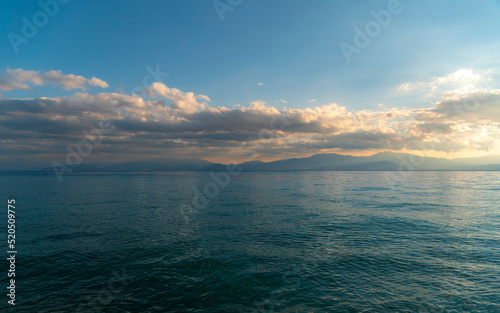 Cloudy sky above the sea and mountains in the horizon's background. The change of weather is continuous in all seasons. Calm, relaxing, scenic view.