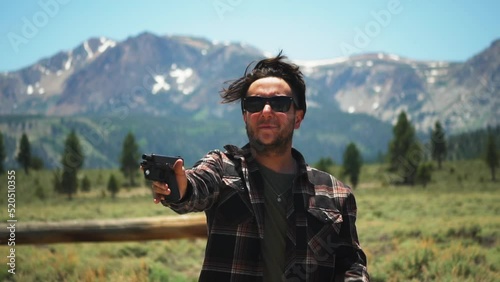 Caucasian gunman points handgun in a picturesque mountain range. fixing hair, gun fails photo