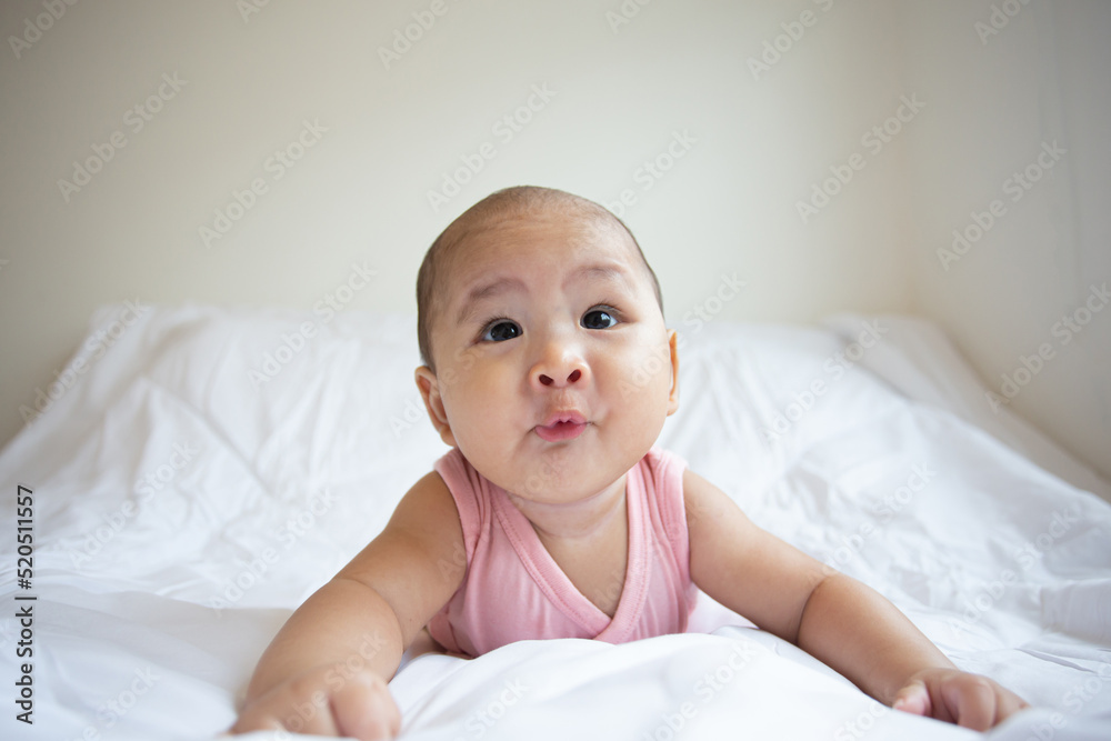 Asian cute baby in white sunny bedroom. Newborn child relaxing on bed