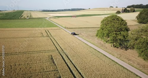 A volvo car drives on a small road between large wheat fields in the countryside, Vaud, Switzerland, high altitude drone view photo