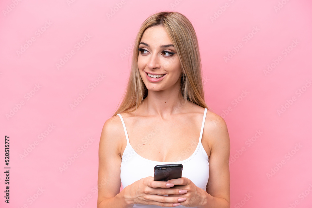 Pretty blonde woman isolated on pink background using mobile phone and looking up