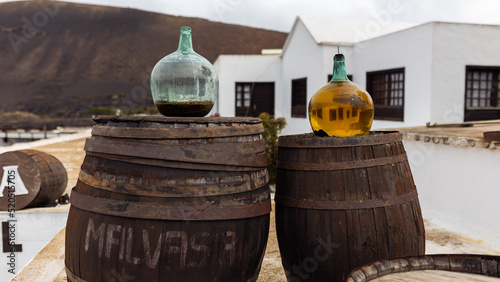 Glass bottles with white volcanic wine - malvasia, standing on vintage wooden barrels against the backdrop of the winery, Lanzarote, Canary Islands, Spain