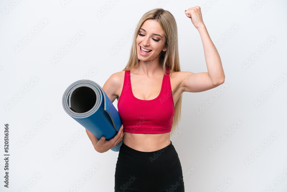 Young sport blonde woman going to yoga classes while holding a mat isolated on white background celebrating a victory Young sport blonde woman going to yoga classes while holding a mat isolated on white background celebrating a victory