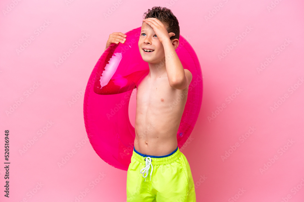 Fototapeta premium Little caucasian boy holding a inflatable donut isolated on pink background smiling a lot