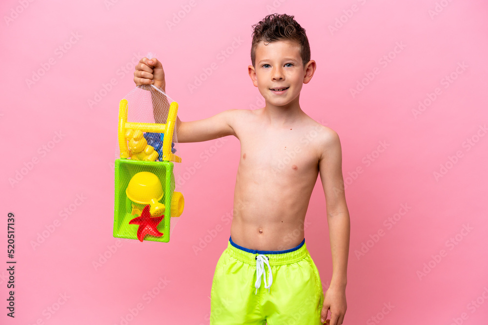Little caucasian boy holding beach toys isolated on pink background smiling a lot Little caucasian boy holding beach toys isolated on pink background smiling a lot