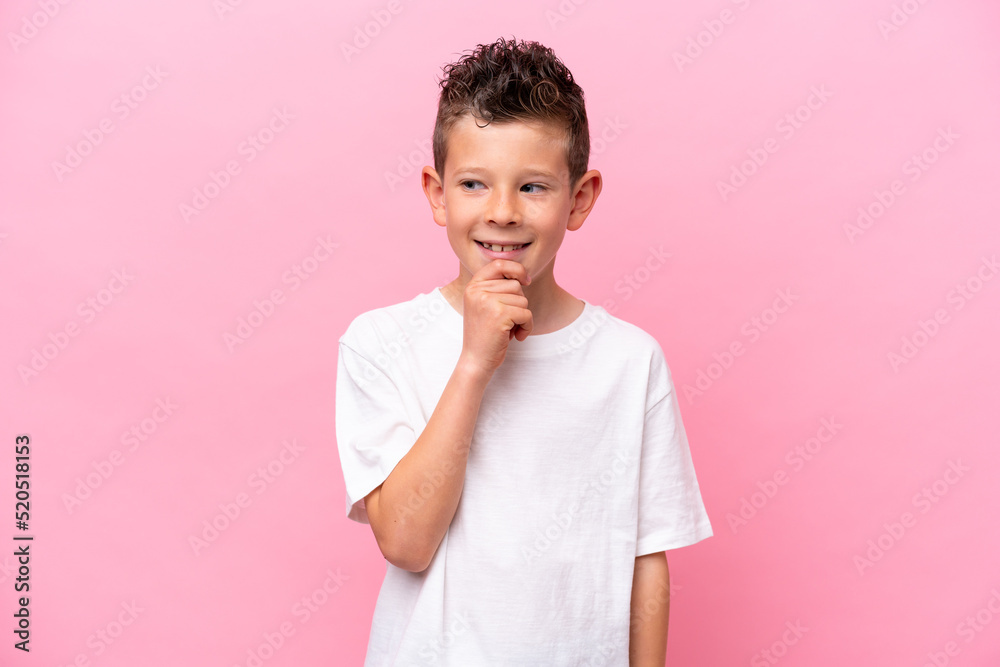 Little caucasian boy isolated on pink background looking to the side and smiling