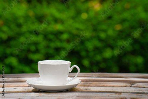 white ceramic coffee mug On the wooden floor, green tree bokeh background.